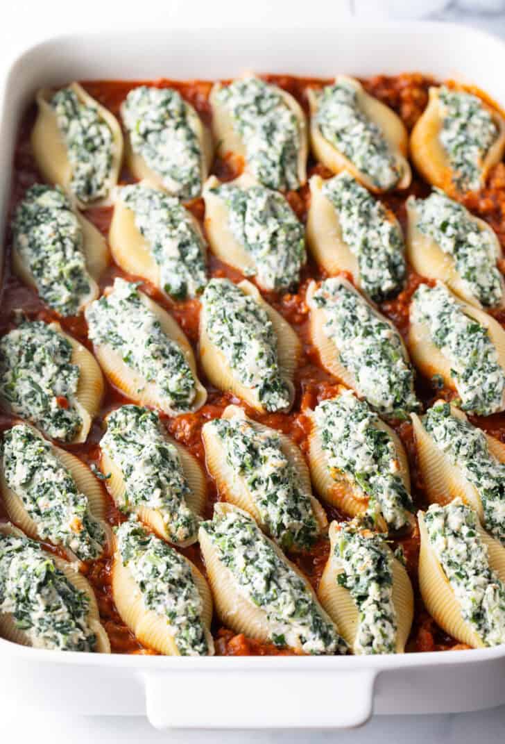25 spinach and meat stuffed shells in a white baking dish, ready to go into the oven