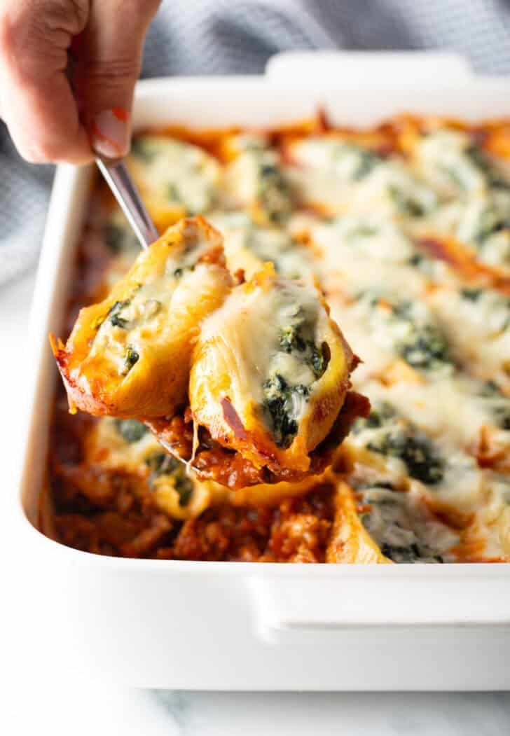 Spoon holding two spinach and cheese stuffed shells to camera.