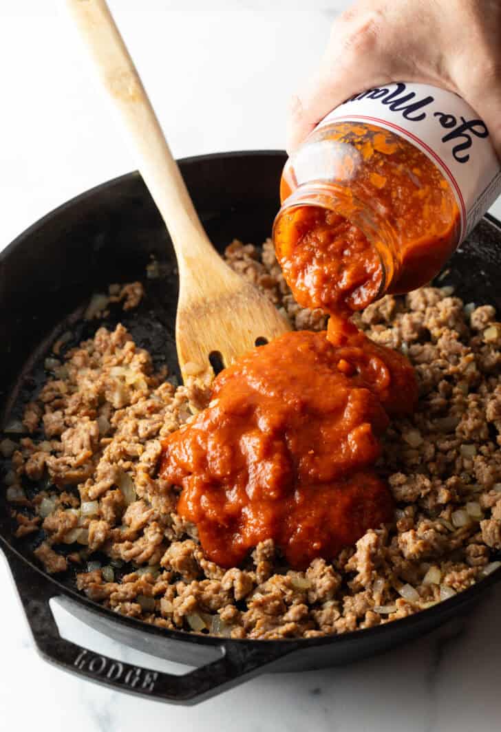 Adding jarred sauce to ground beef in a skillet.