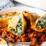 4 stuffed shells with spinach and meat sauce on a white plate.