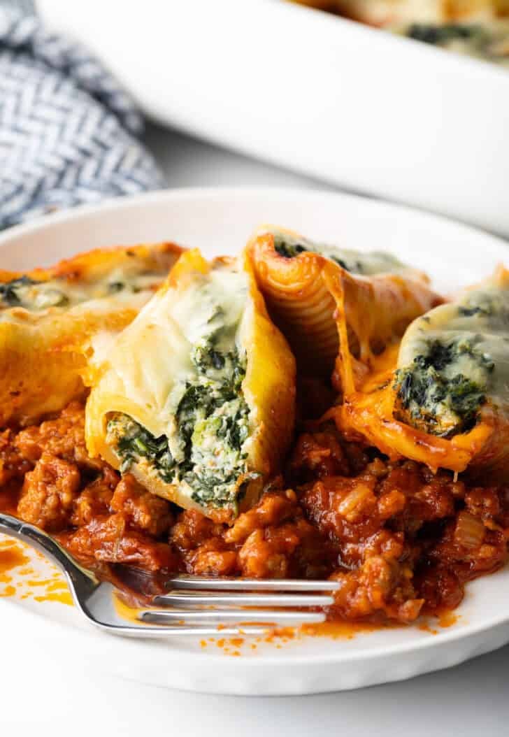 4 stuffed shells with spinach and meat sauce on a white plate.