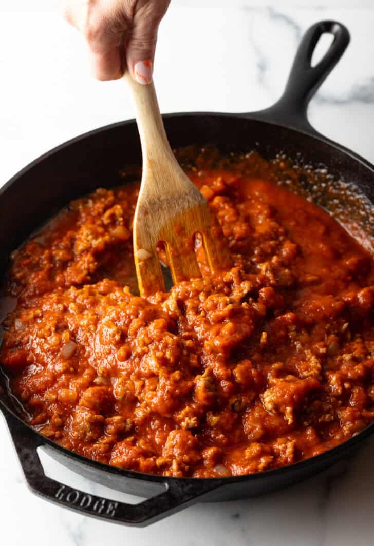 Using a wooden spatula to stir meat sauce in a cast iron skillet.