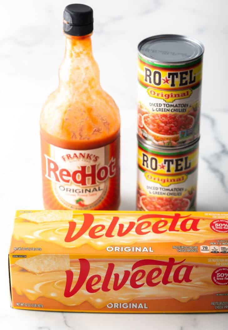 Block of velveeta cheese, bottle of Frank's RedHot sauce, and two cans of rotel chiles stacked on top of each other.
