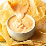 Hand dipping a chip into a white bowl of velveeta cheese dip surrounded by tortilla chips.