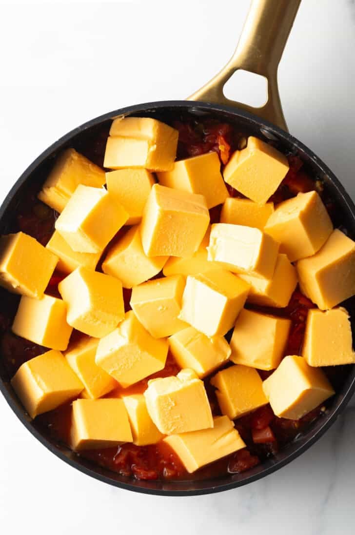 Cubes of velveeta cheese in a deep black skillet.