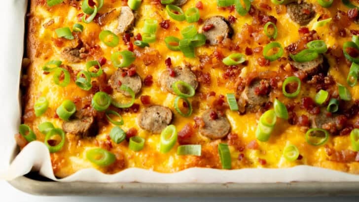 Rectangle baking sheet tray with breakfast pizza, loaded with cheese, sausage, and green onions.