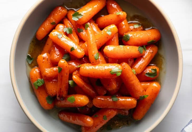 Top down bowl of glazed honey baby carrots sprinkled with chopped parsley.