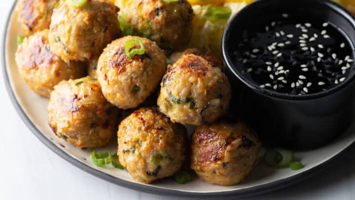 Plate covered half Thai turkey meatballs, dipping sauce, and half chopped Asian salad, plus a black ramekin of dipping sauce.