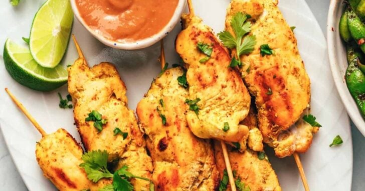 Several chicken satay skewers and bowl of peanut sauce.
