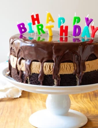 Chocolate and caramel ice cream layered cream cake coated with glossy icing and Happy Birthday candles on top.