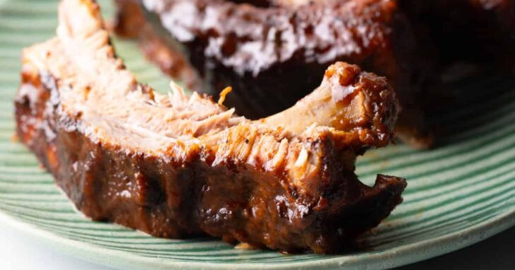 Close up of a saucy pork rib on a green plate.