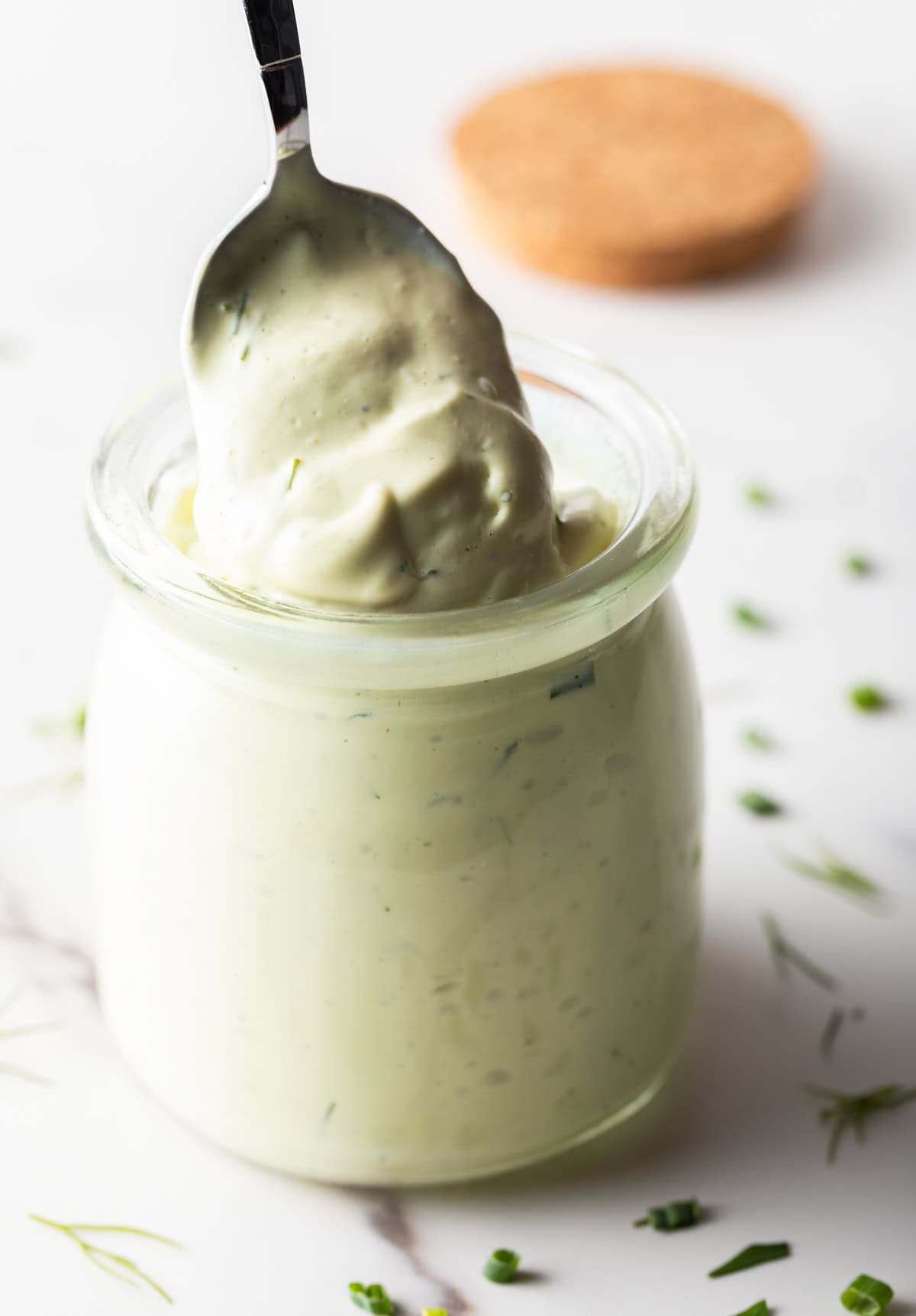 A spoon is scooping a serving of avocado ranch dressing from a glass jar.