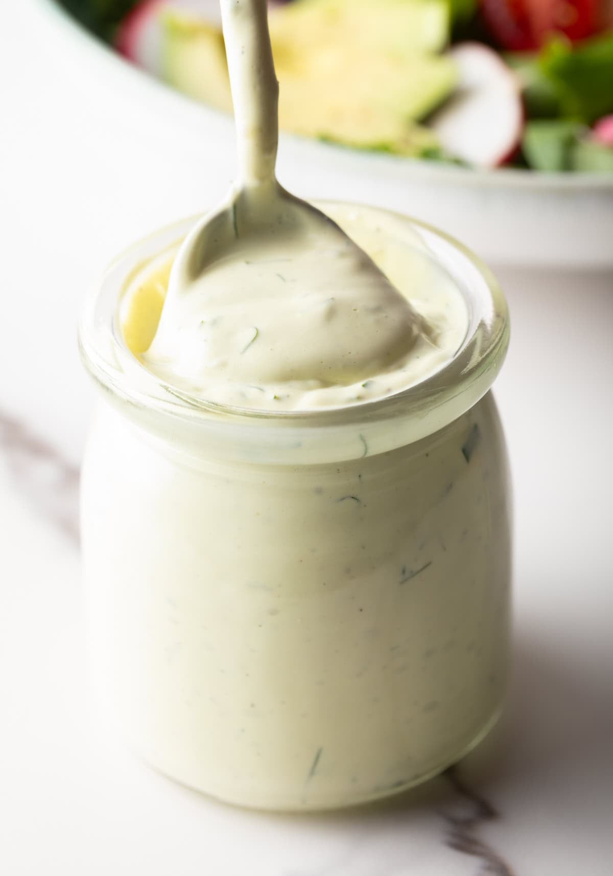 A jar filled with creamy avocado lime ranch dressing, with a spoon scooping a serving.
