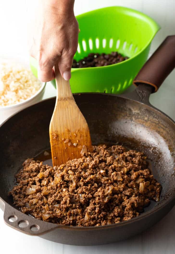 Cooking ground beef in a large skillet with a wooden spoon.