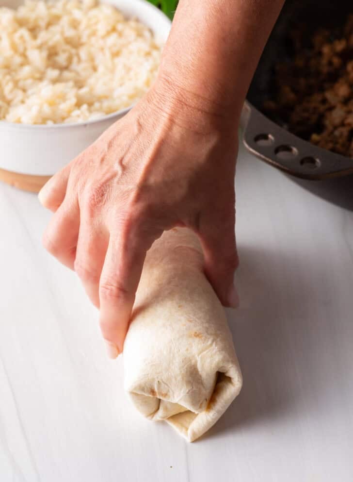 Hand wrapping a beef burrito.