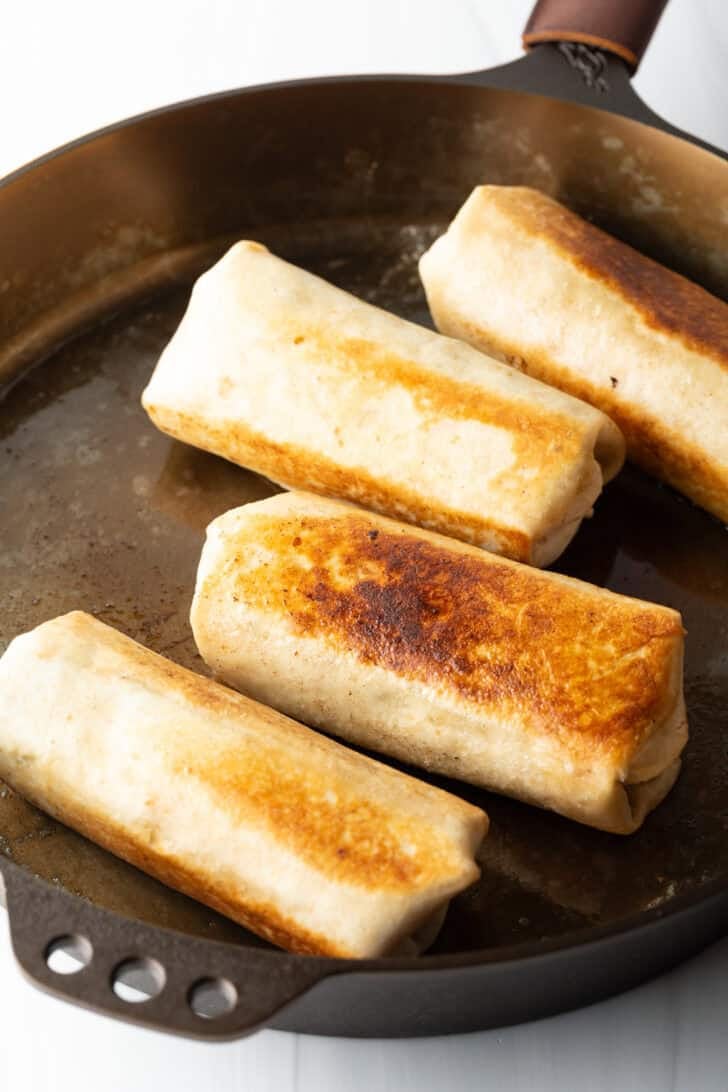 Four seared burritos on a large pan.