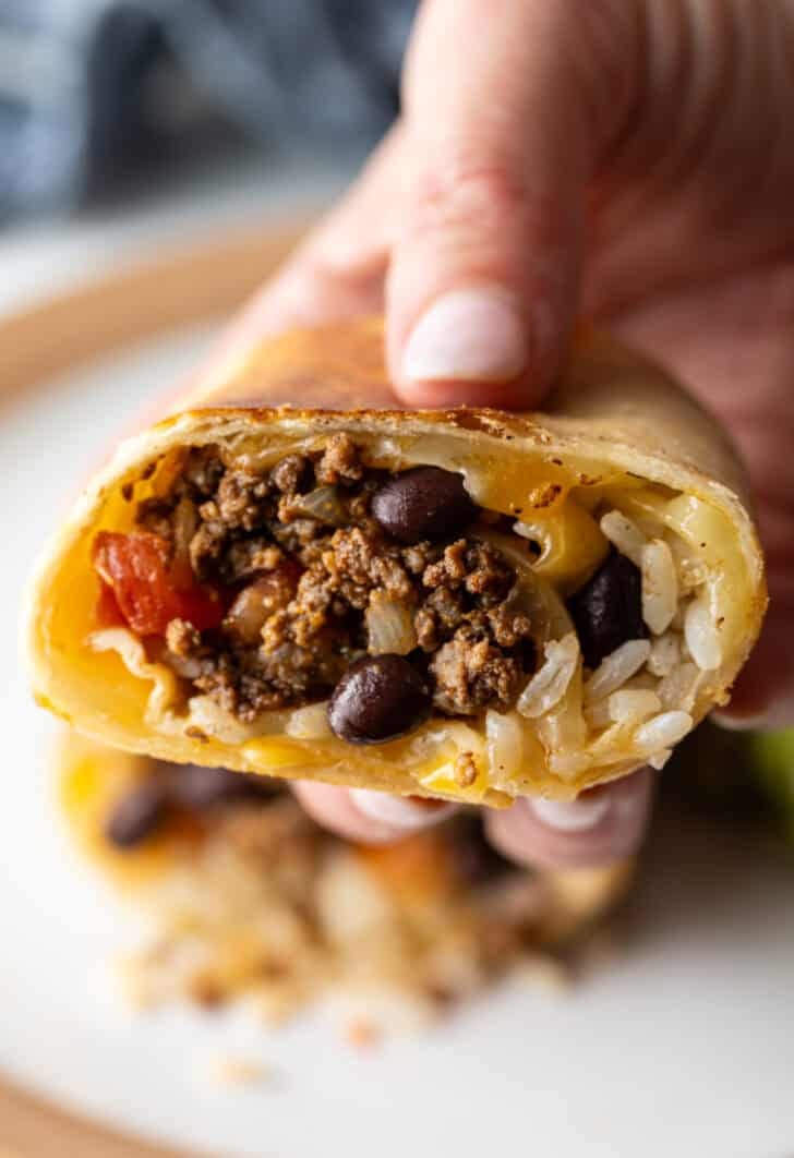 Hand holding the cut side of a beef burrito to camera.