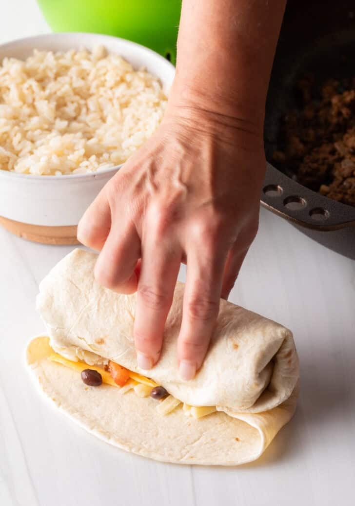 Hand wrapping a beef burrito.