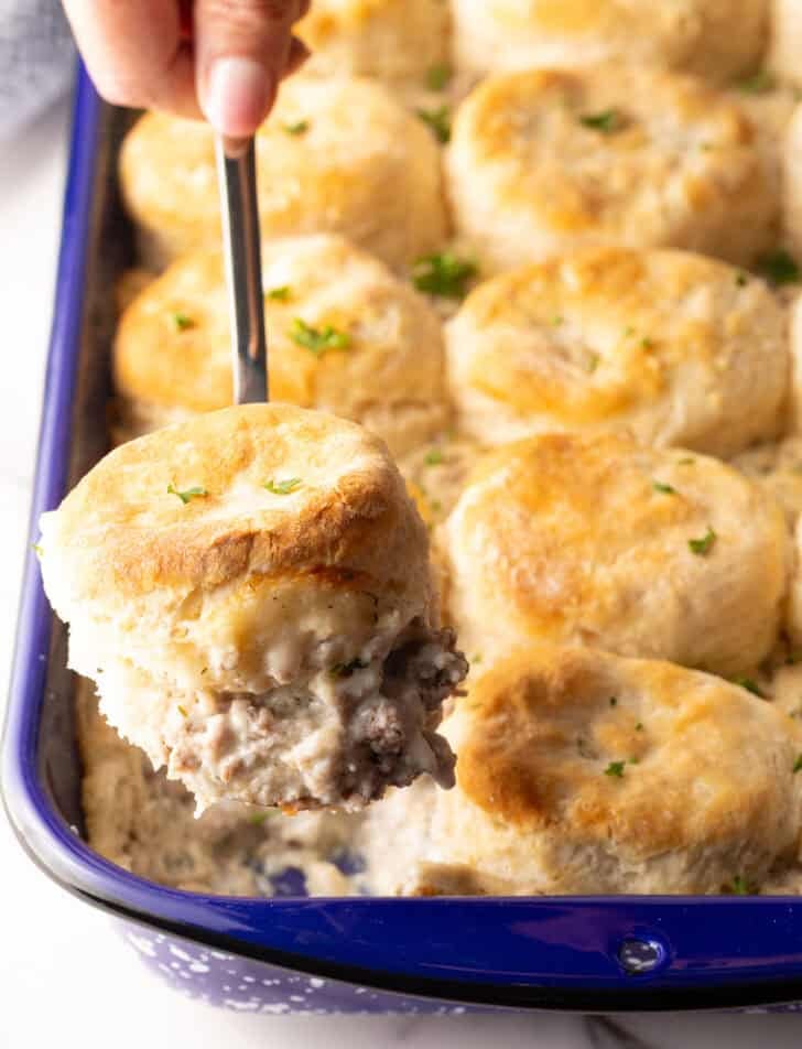A metal spatula taking a scoop of biscuits and gravy breakfast casserole from the pan.