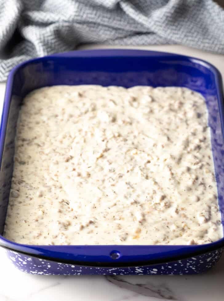 Sausage gravy layered on the bottom of a blue baking pan.