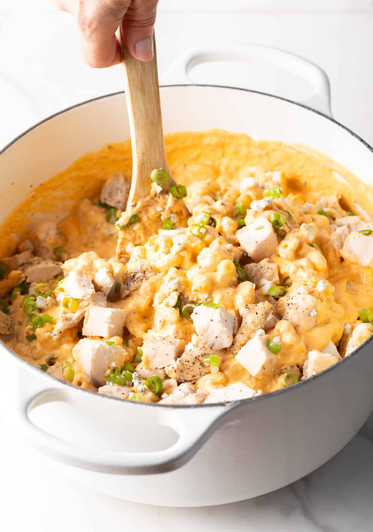 Using a wood spoon to stir cooked chopped chicken in a pot of macaroni and cheese.