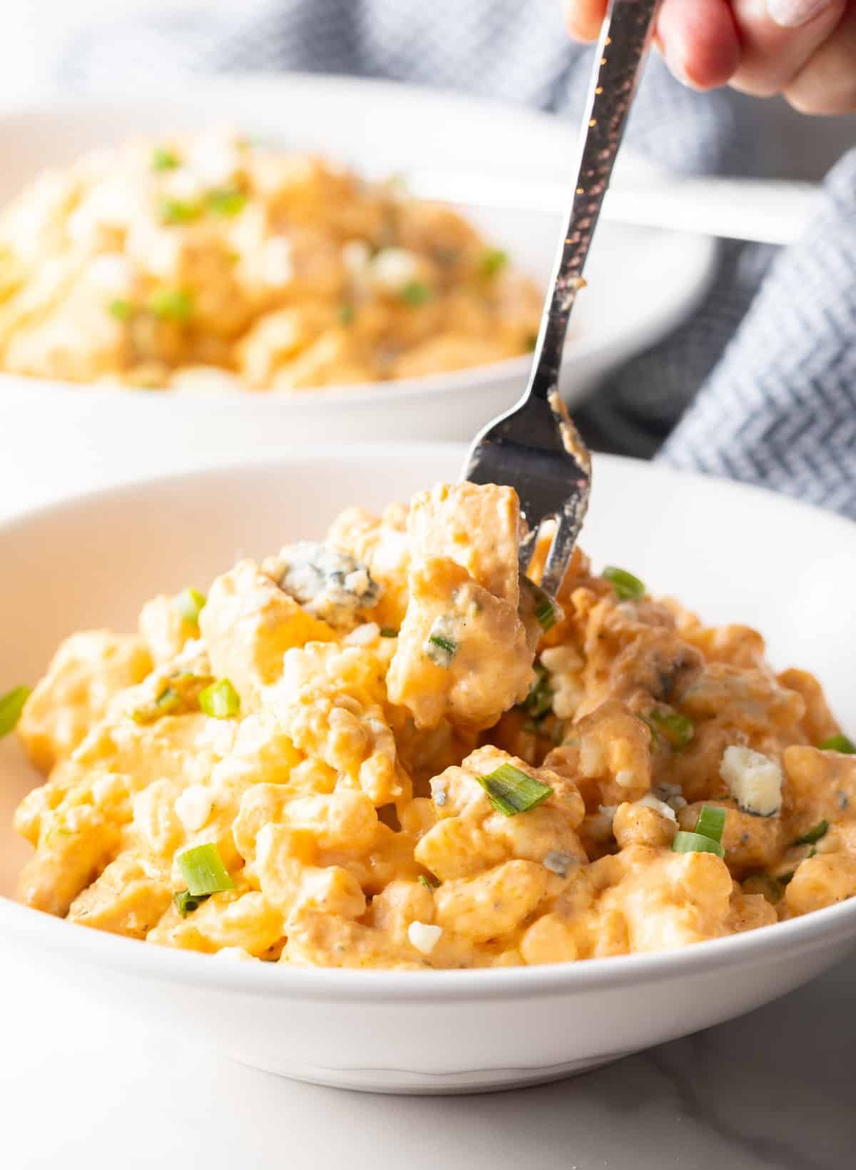 Fork taking a bite of buffalo macaroni and cheese from a white bowl.