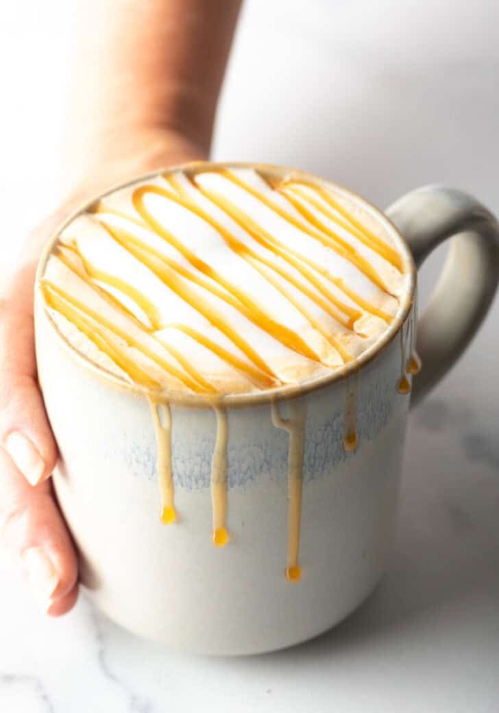 Hand holding white mug filled with caramel macchiato and caramel drizzle.