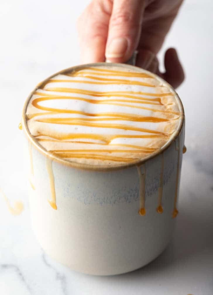 Hand holding white mug filled with caramel macchiato and caramel drizzle.