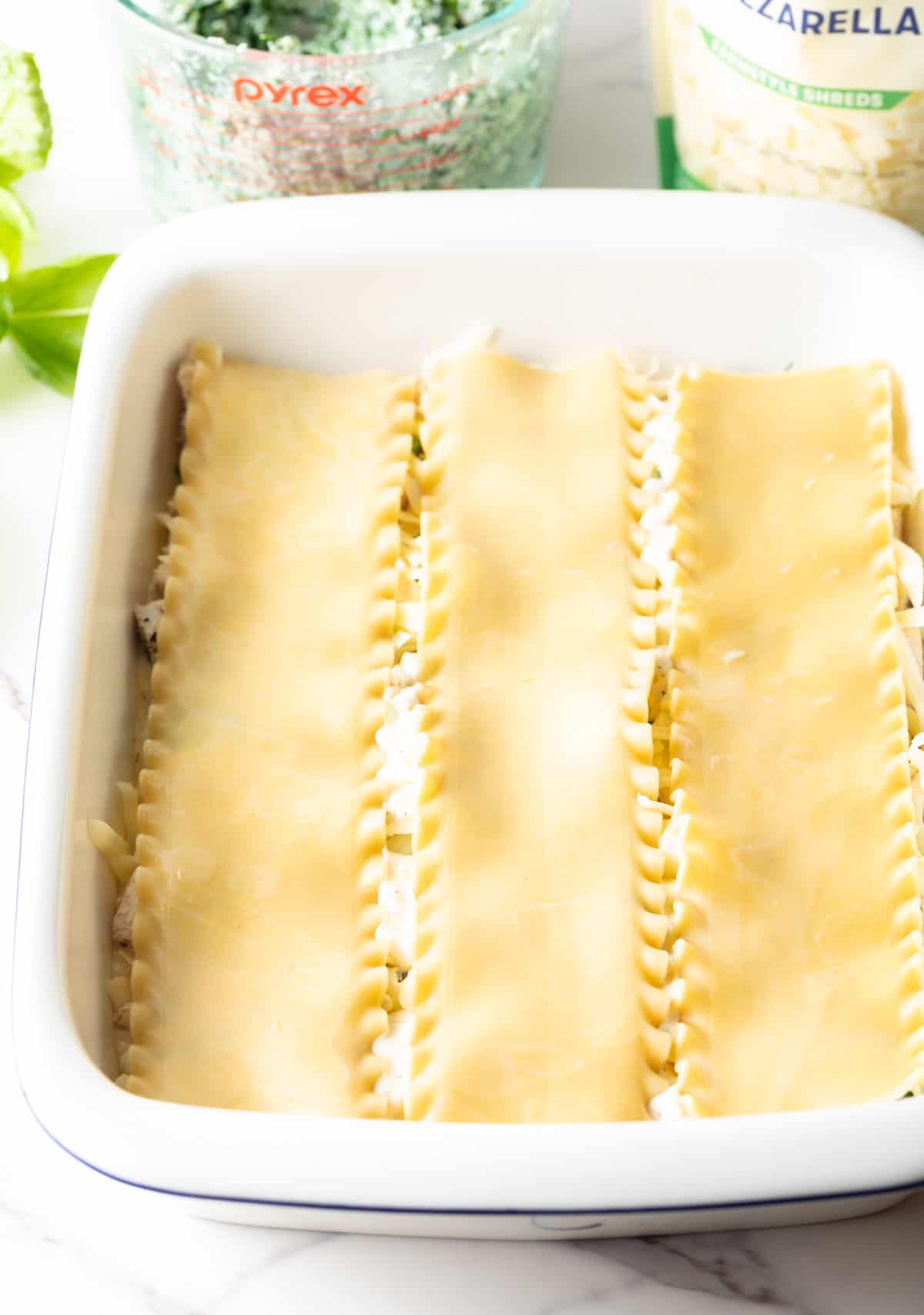 Layering lasagna noodles in a white rectangle casserole dish.