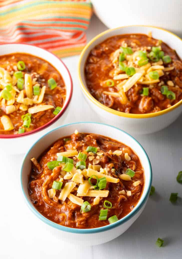 3 bowls of chicken chili, topped with chopped green onion and shredded cheddar cheese.