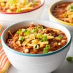 Bowlful of chicken chili, topped with chopped green onion and shredded cheddar cheese.