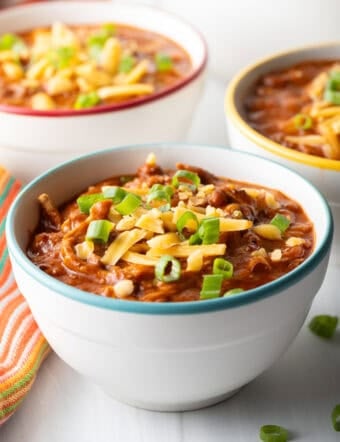 Bowlful of chicken chili, topped with chopped green onion and shredded cheddar cheese.
