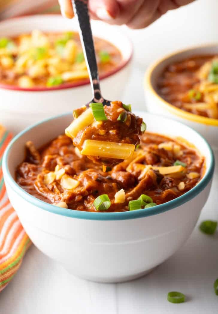 Spoon digging into a white bowl of shredded chicken, bean and salsa chili.