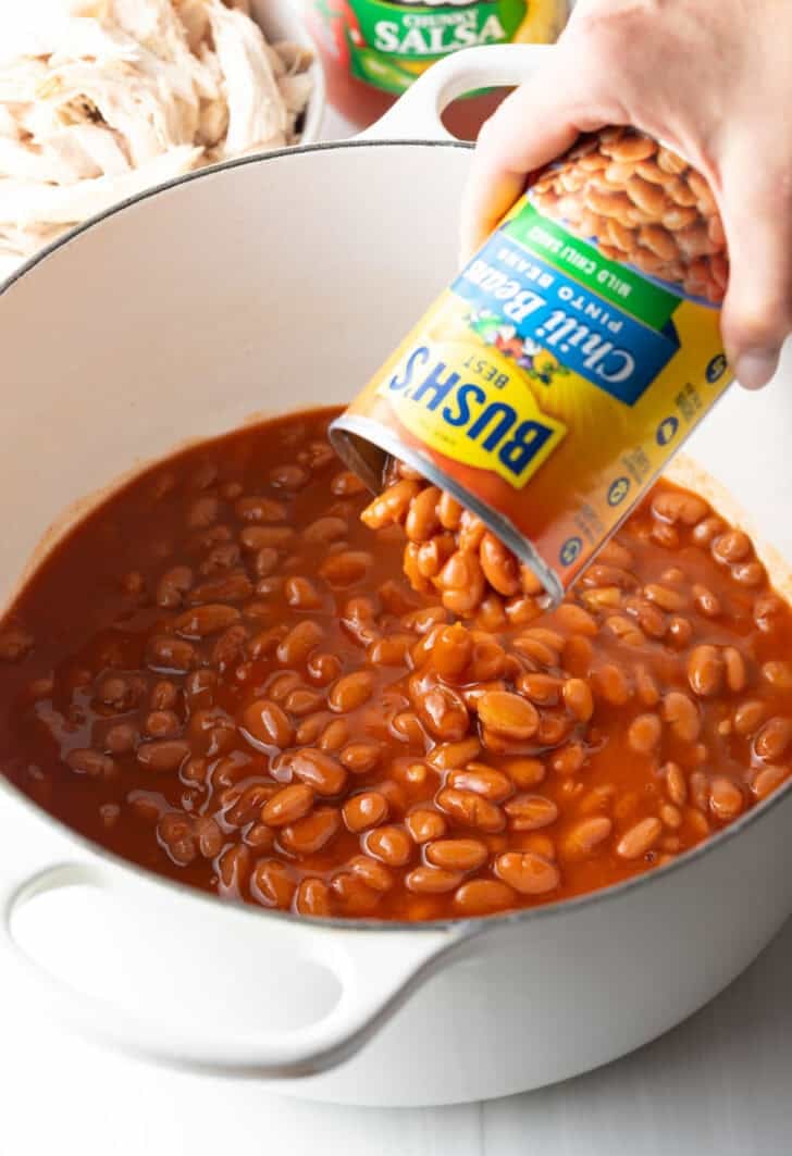Adding pinto beans from a can into a pot of enchilada sauce.