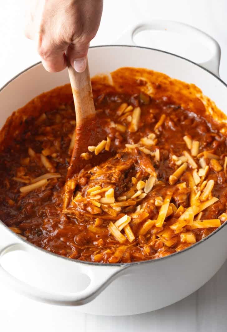Using a wood spoon to stir shredded cheese into a pot of chili.