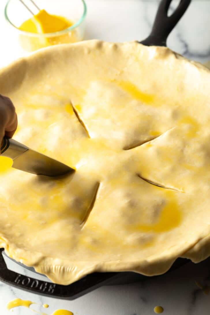 Pie crust being prepped for baking with a knife cutting slits in the top.