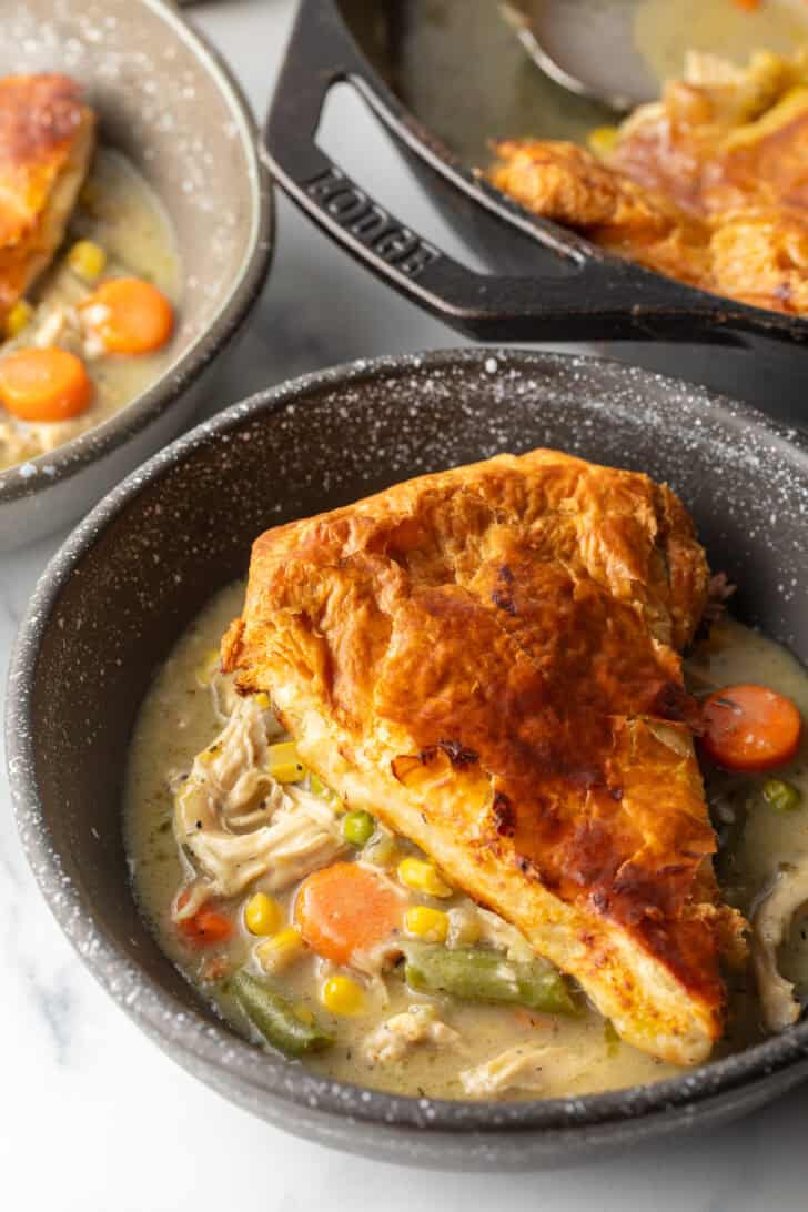 Top down view of a wedge of chicken pot pie with puff pastry crust on a black plate.