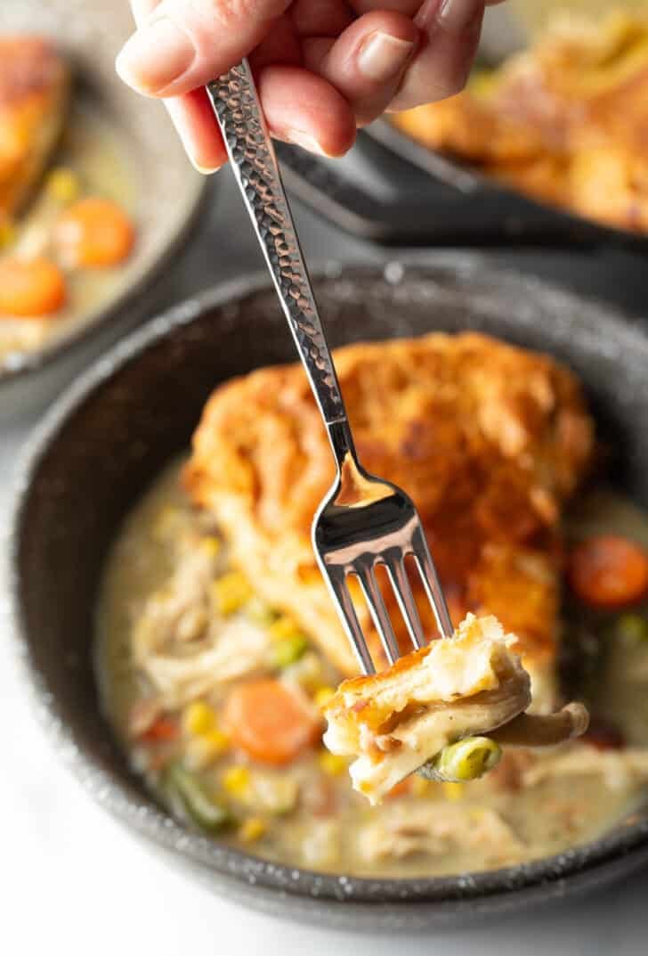 Fork holding a bite of chicken pot pie to camera.