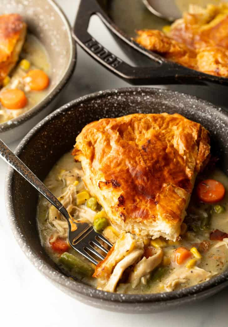Top down view of a wedge of chicken pot pie with puff pastry crust on a black plate with a fork.
