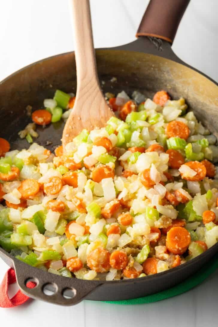 Sauteeing chopped carrots, celery, and onion in a cast iron skillet.