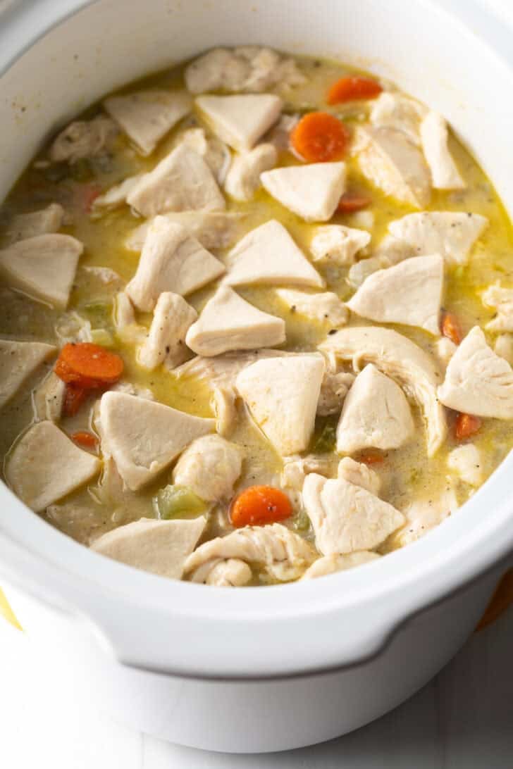 Triangles of biscuit dough added to a white slow cooker with chicken and broth.
