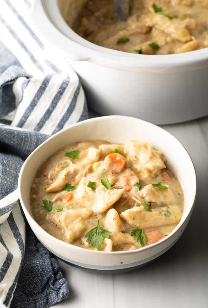 White bowl with crock pot chicken and dumplings sprinkled with fresh chopped parsley.