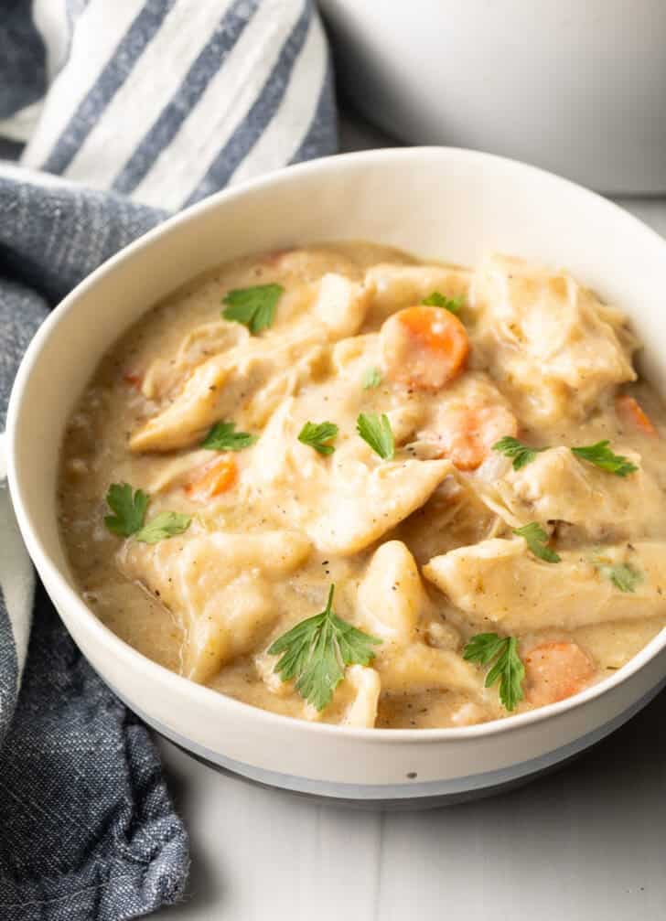 White bowl with crock pot chicken and dumplings sprinkled with fresh chopped parsley.