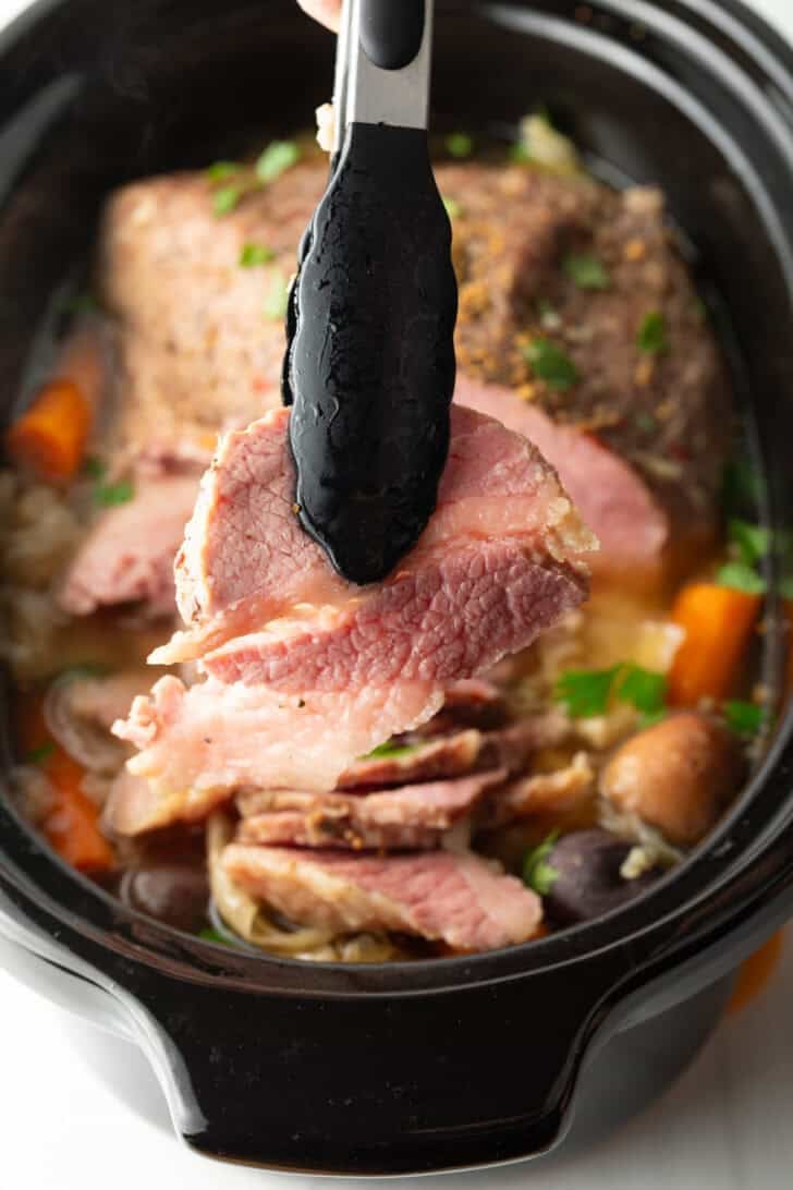 Tongs holding a piece of corned beef to the camera.