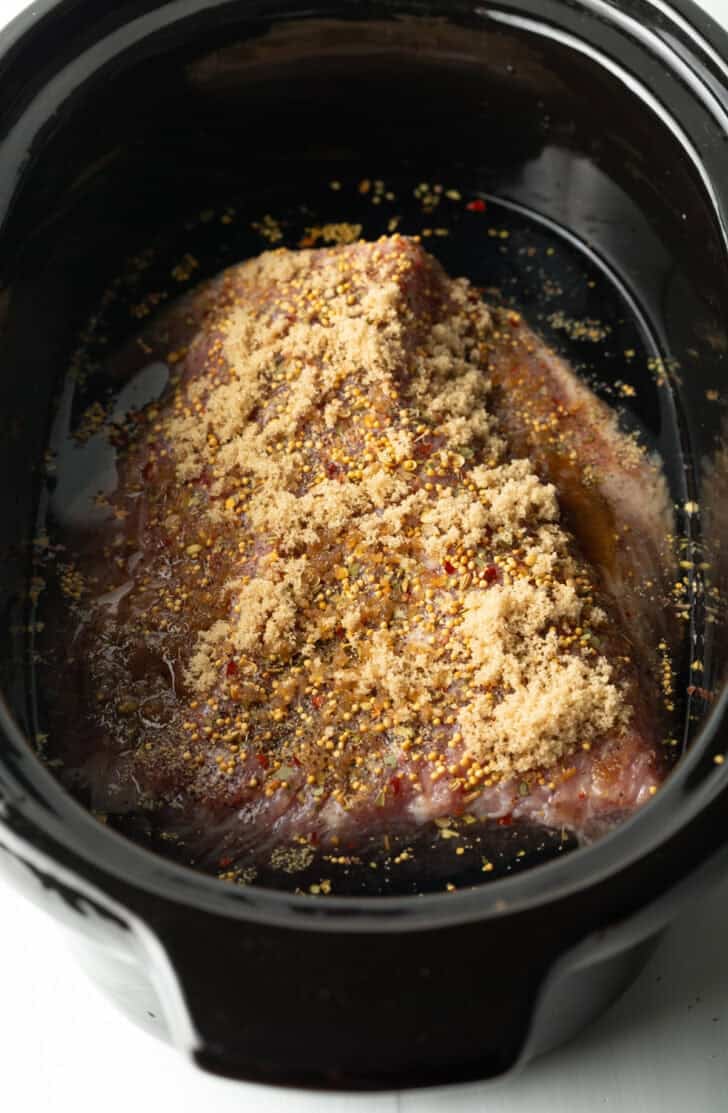 Whole seasoned beef brisket in a black slow cooker.