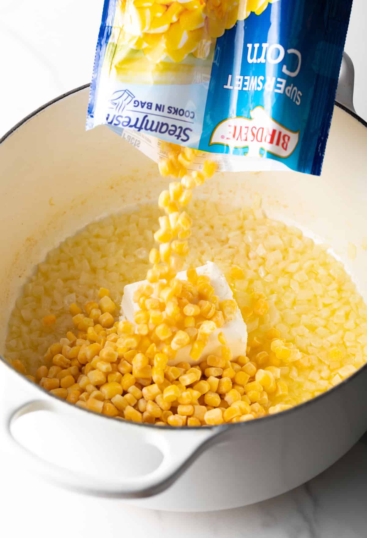 Adding frozen corn from a bag into a large pot of corn with butter.