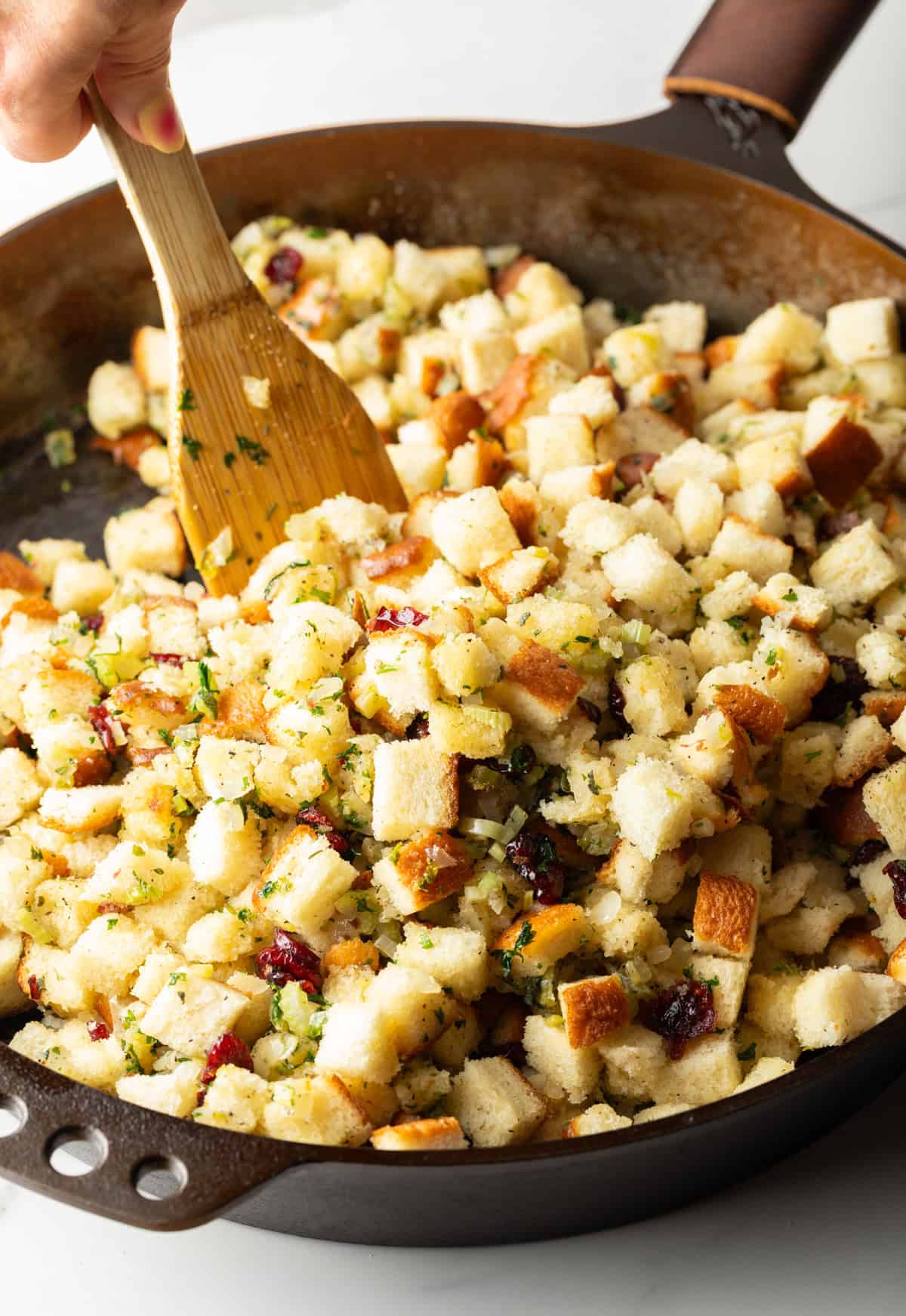 Using a wooden spatula to stir bread cubes around a deep skillet.