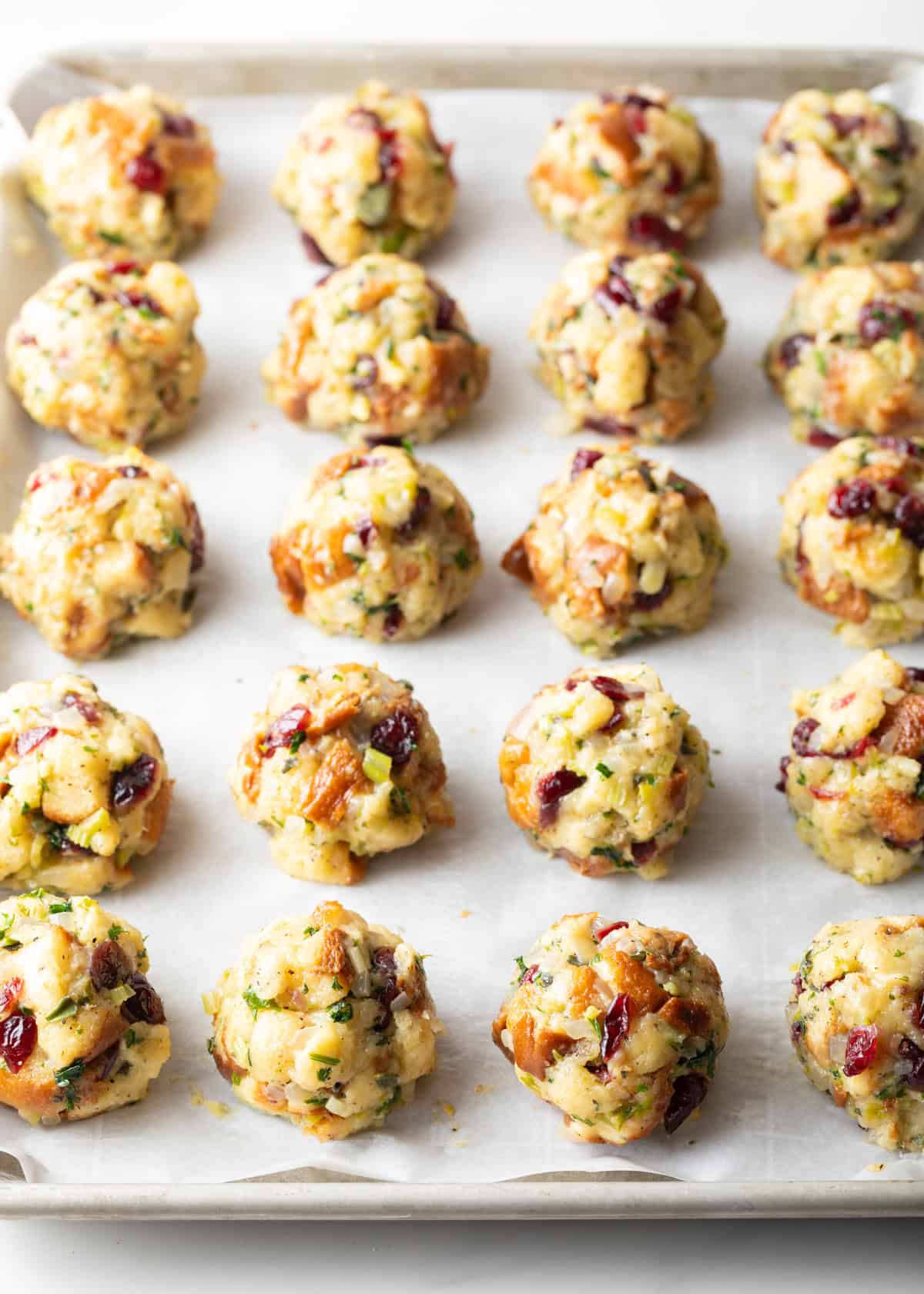 20 unbaked stuffing balls in rows on a baking sheet.