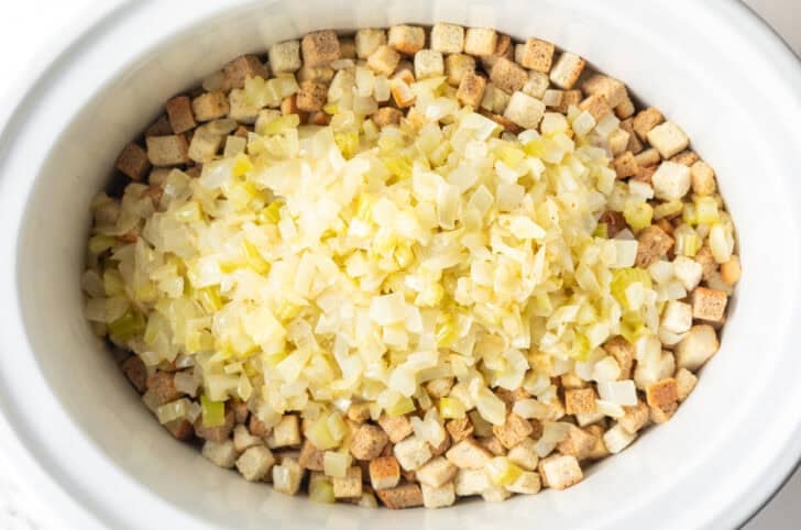 Dried bread cubes topped with cooked onions in a white crock pot.
