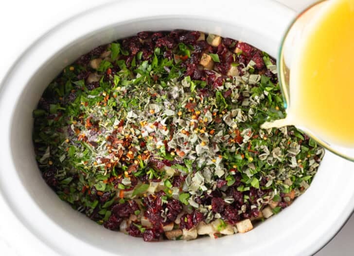 Broth pouring over slow cooker stuffing recipe before cooking.